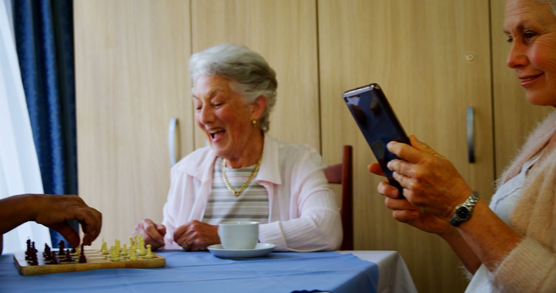 Smiling elderly women playing chess while sitting at table with friends - Free Images, Stock Photos and Pictures on Pikwizard.com