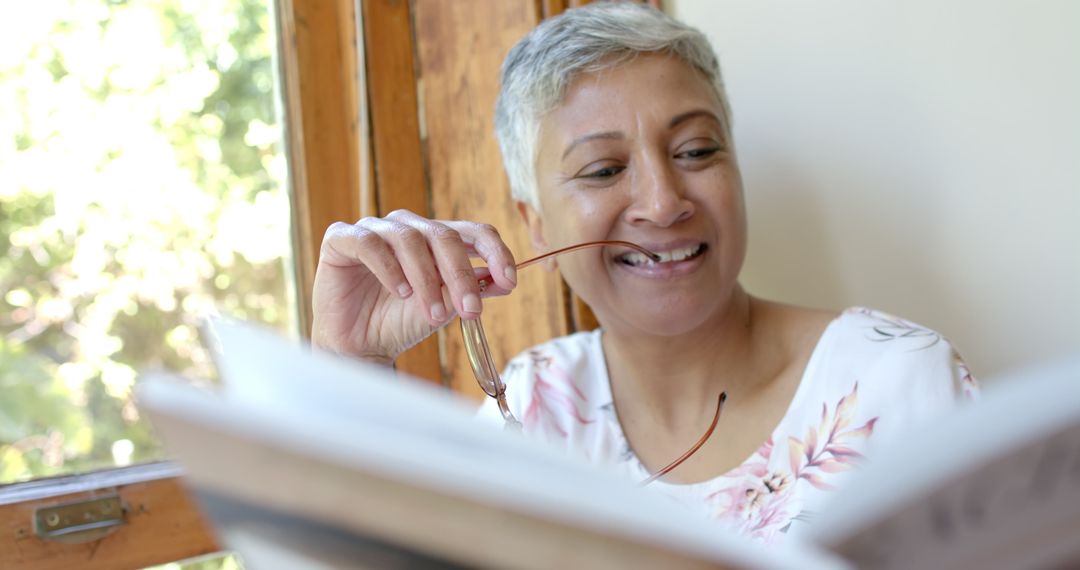 Happy Senior Woman Relaxed Reading by Window in Bright Home