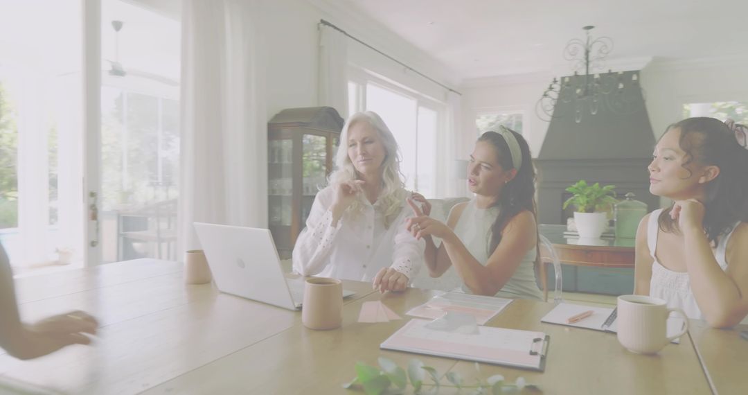 Intergenerational family discussing plans around laptop at sunny dining table with coffee