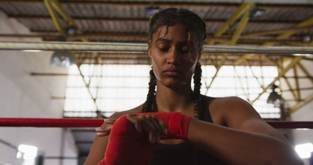 Focused biracial female boxer with braids wrapping hands sitting by ...