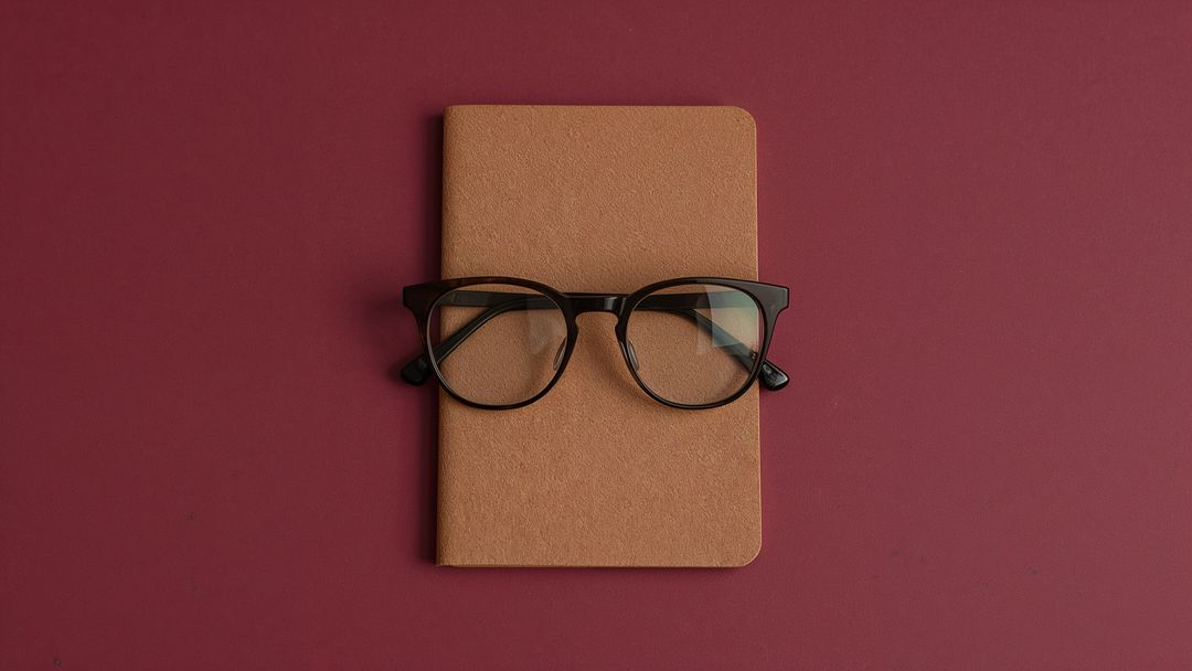 Minimalist Brown Notebook with Black Glasses on Maroon Background