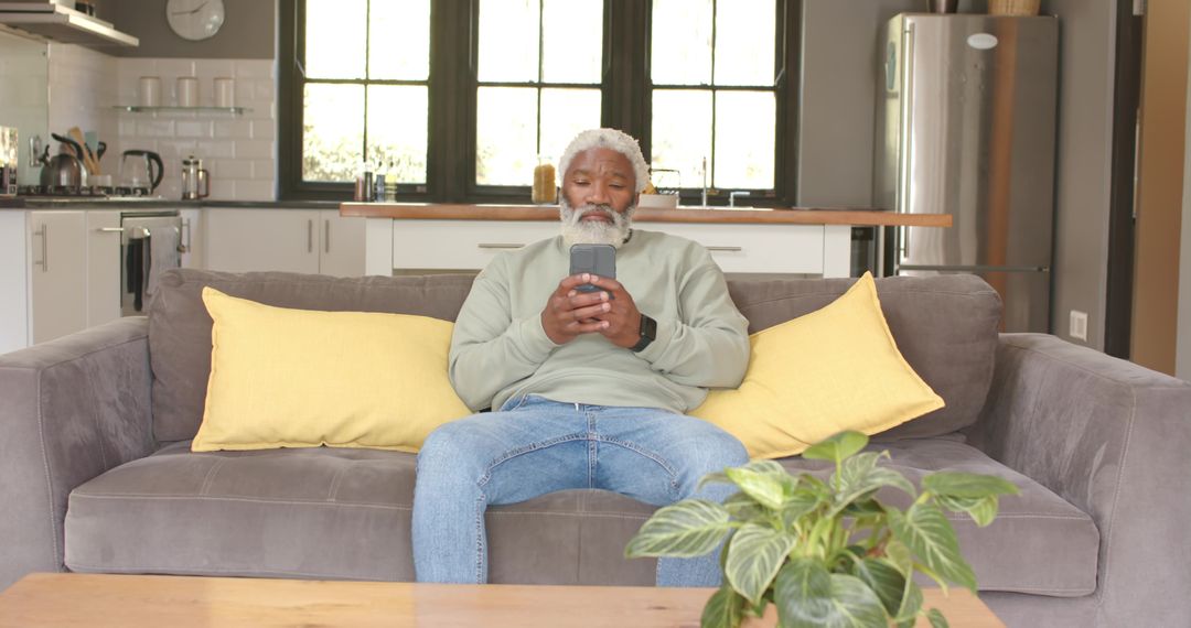 Mature Man Relaxing on Couch Using Smartphone in Contemporary Kitchen