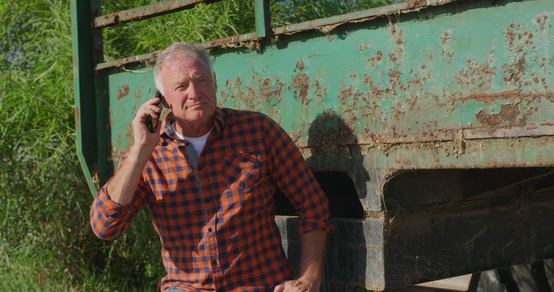 Elderly Farmer Using Mobile Phone by Rusty Trailer - Free Images, Stock Photos and Pictures on Pikwizard.com