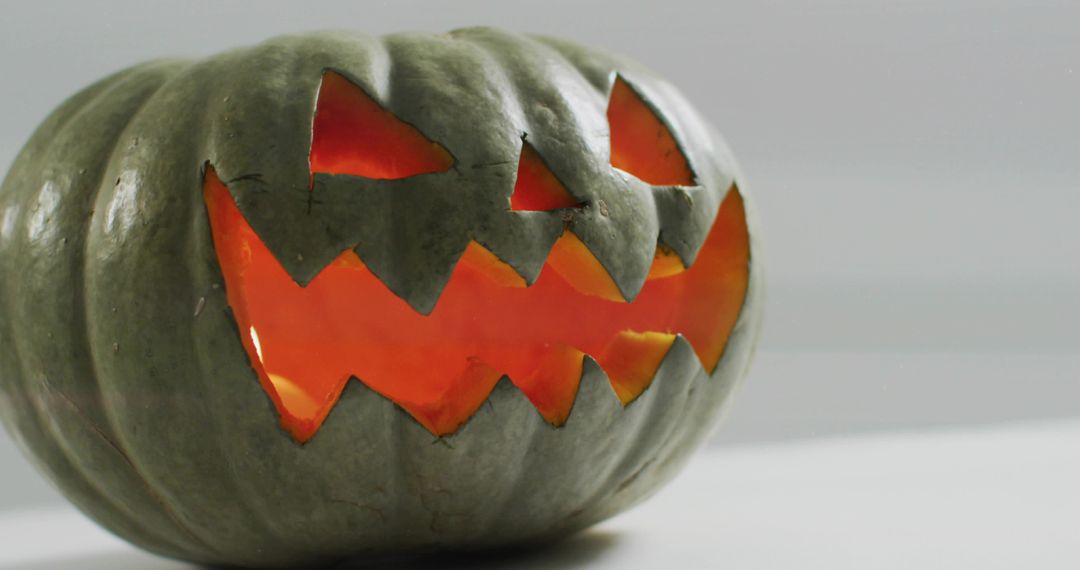 Glowing carved green pumpkin casting warm orange light and soft shadow