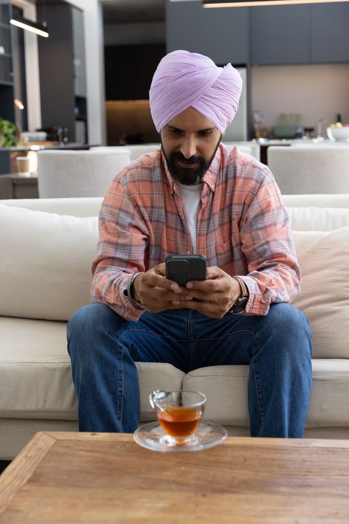 Indian Man Wearing Lavender Turban Using Smartphone in Cozy Home
