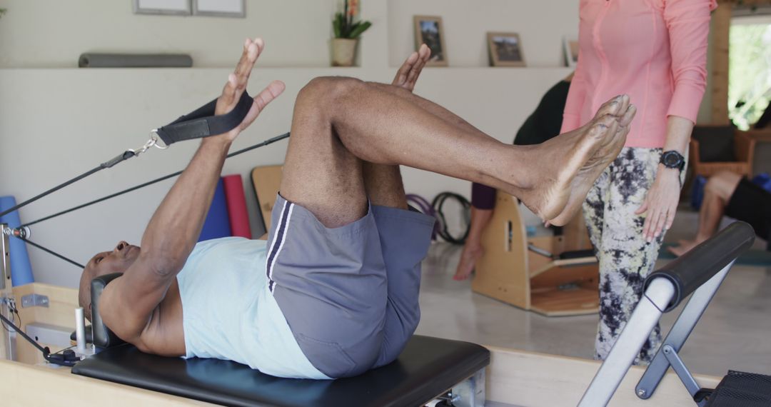 Man Exercising on Pilates Reformer with Trainer Assistance - Free Images, Stock Photos and Pictures on Pikwizard.com