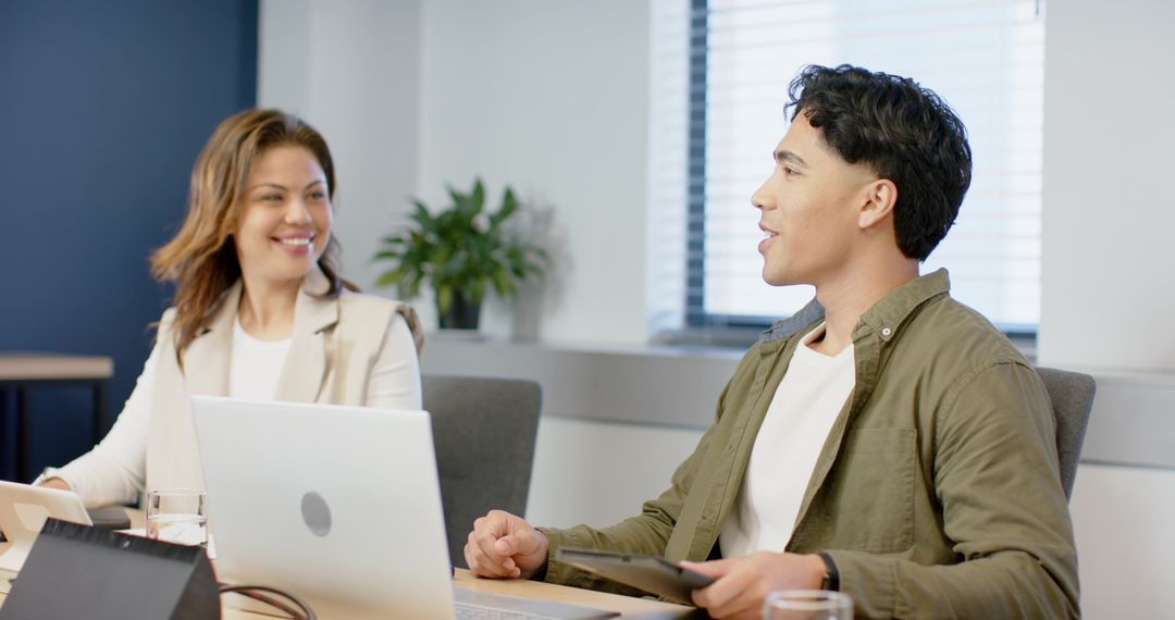 Two colleagues collaborating in meeting room with laptops and tablet for office teamwork