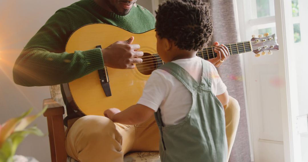 Image of light flashing over happy african american father and son playing guitar - Free Images, Stock Photos and Pictures on Pikwizard.com