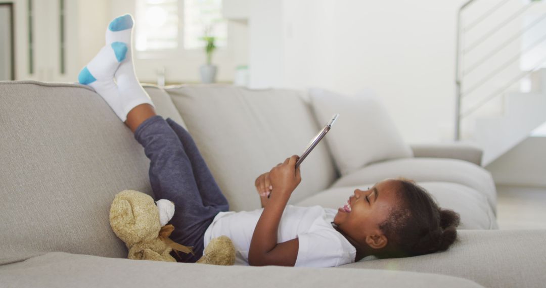 Laughing Child Using Tablet on Sofa at Home