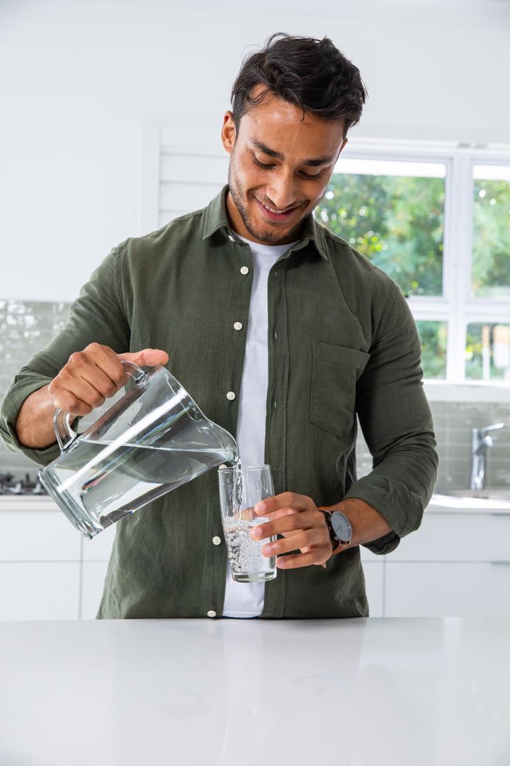 Man Pouring Water into Glass in Modern Kitchen
