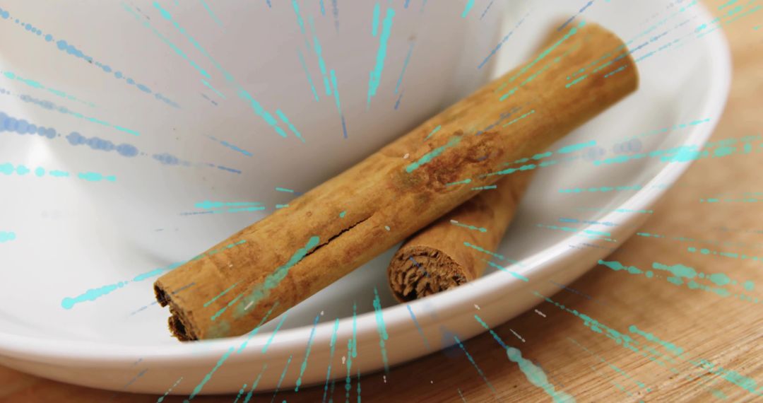 Cinnamon sticks resting in white ceramic bowl with teal paint splashes on wooden surface