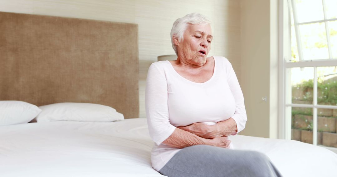 Elderly Woman Experiencing Stomach Pain Sitting on Bed - Free Images, Stock Photos and Pictures on Pikwizard.com