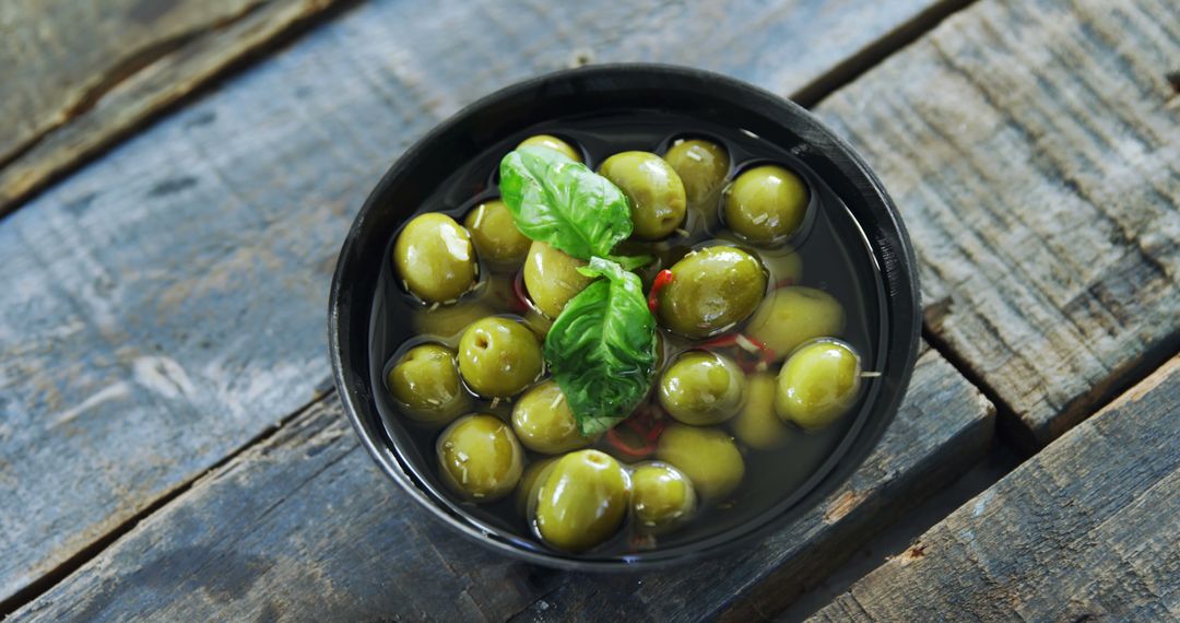 Mediterranean Green Olives in Black Bowl with Basil on Rustic Wooden Table - Free Images, Stock Photos and Pictures on Pikwizard.com