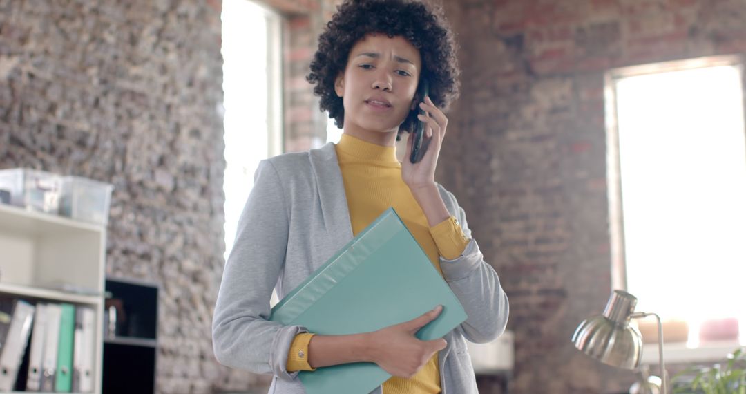 Young Professional Woman in Office Holding Folder While Talking on Phone - Free Images, Stock Photos and Pictures on Pikwizard.com