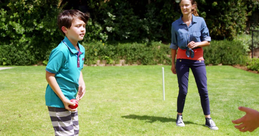 Young boy holding ball with woman supervising outdoor yard game - Free Images, Stock Photos and Pictures on Pikwizard.com