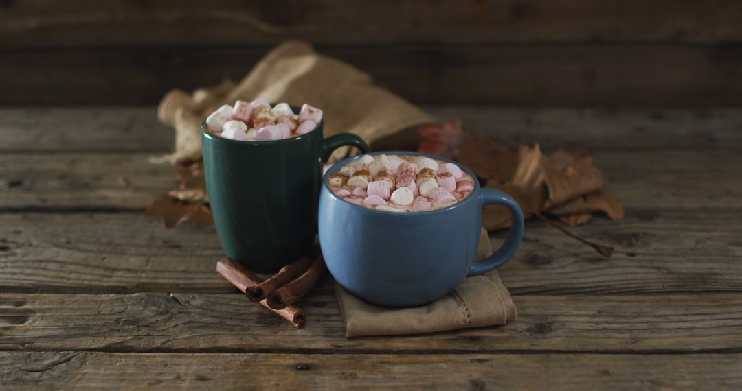 Two cups of hot chocolate with marshmallows, autumn leaves and cinnamon sticks on wooden surface - Free Images, Stock Photos and Pictures on Pikwizard.com