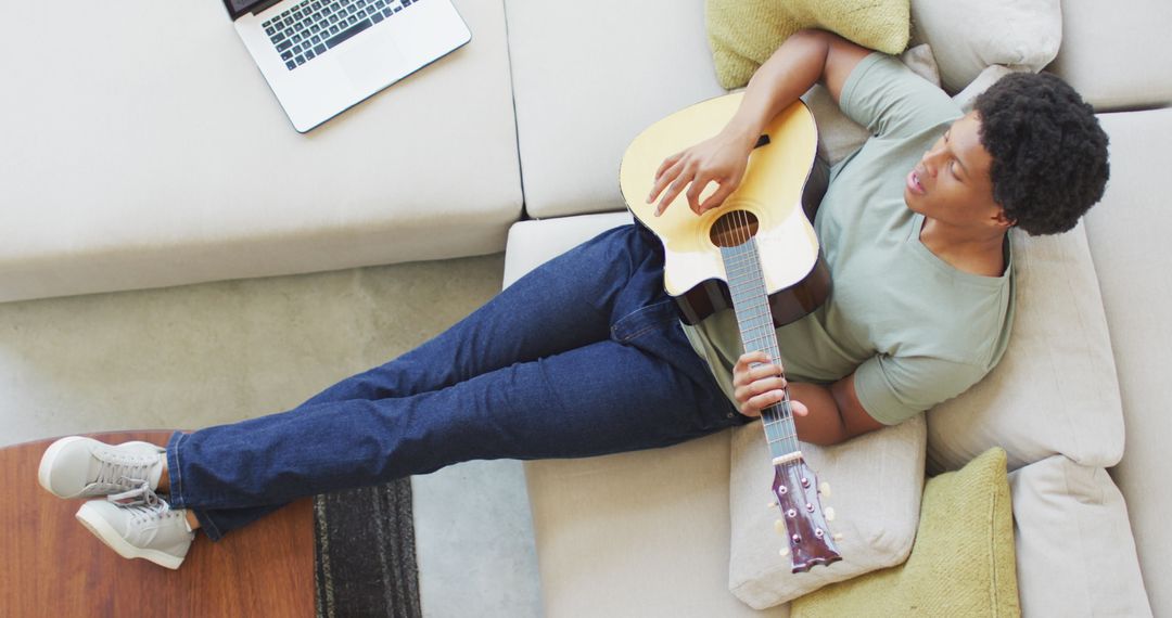 Man Relaxing on Sofa Playing Guitar During Leisure