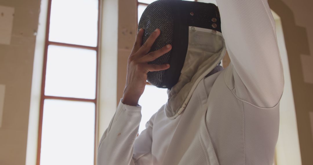 Fencing Athlete Adjusting Helmet in Sunlit Room - Free Images, Stock Photos and Pictures on Pikwizard.com