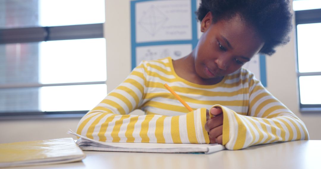 Young Girl Focused on Writing in Classroom Setting Near Window