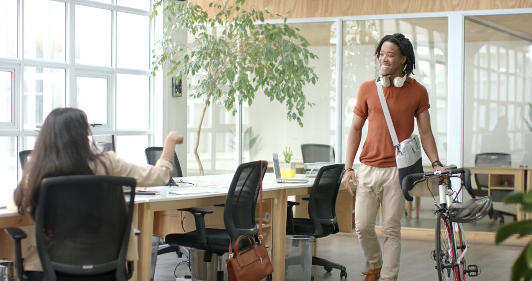 Young Black Professional Walking Bicycle into Bright Open Office While Greeting Coworker