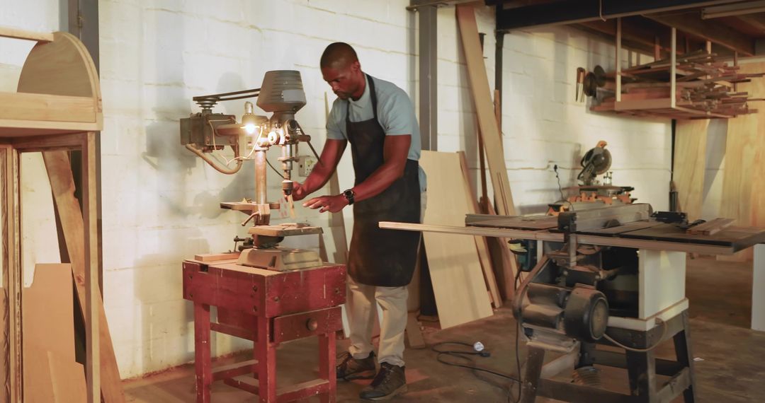 Mature African American Carpenter Working at Drill Press in Rustic Woodshop with Table Saw