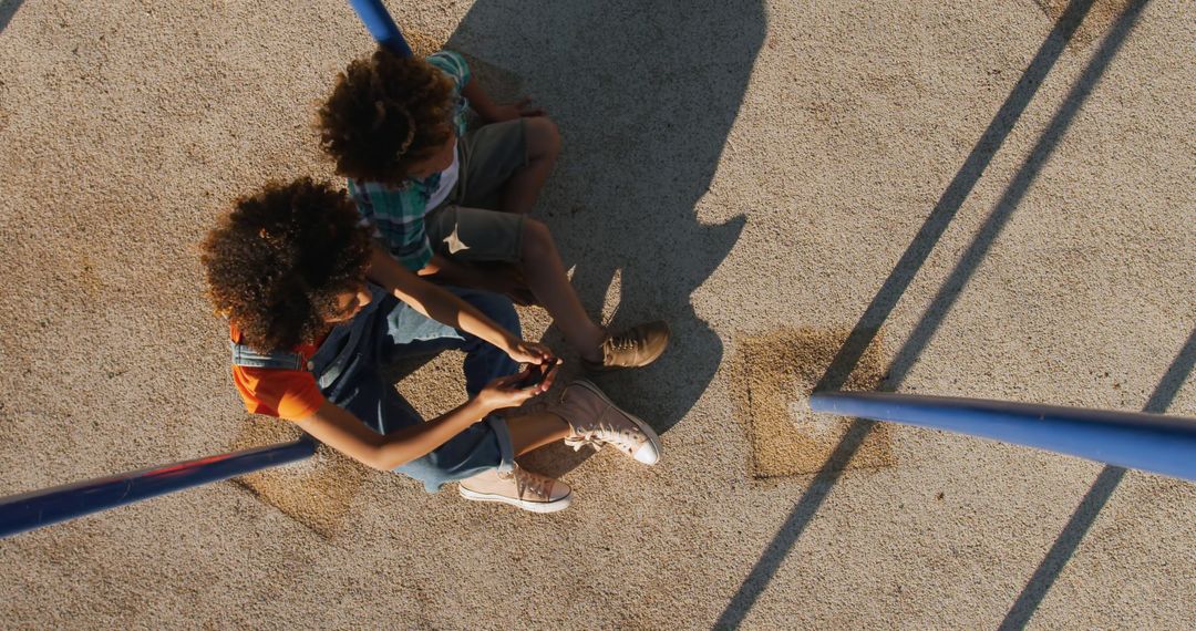 Top View of Two Children Sitting Together on Playground - Free Images, Stock Photos and Pictures on Pikwizard.com