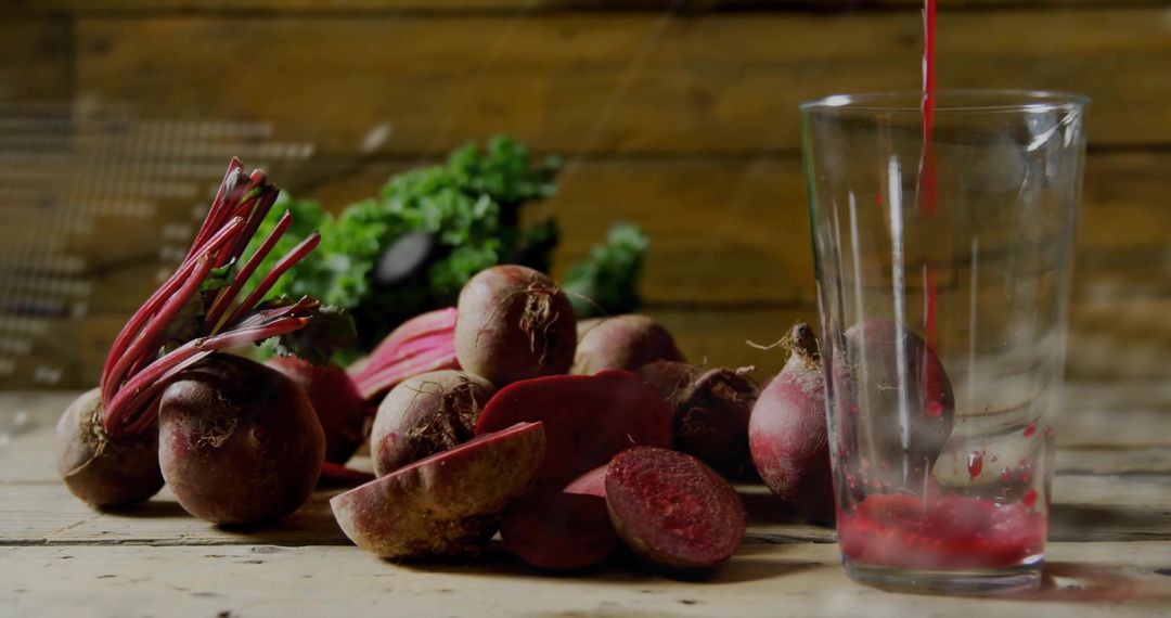 Pouring beet juice into tall glass with fresh halved beets on rustic wooden table