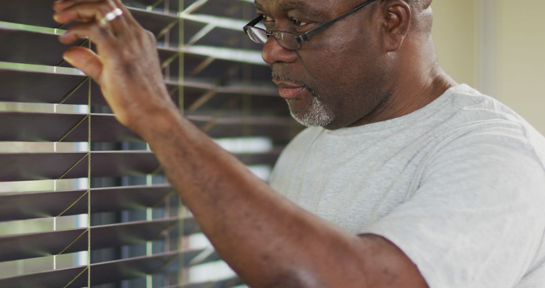 African american senior man looking through blinds out of the window and smiling - Free Images, Stock Photos and Pictures on Pikwizard.com