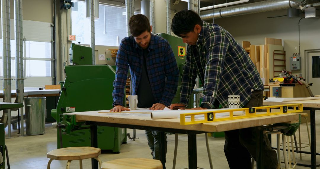 Two Male Woodworkers Discussing Blueprints in Workshop - Free Images, Stock Photos and Pictures on Pikwizard.com