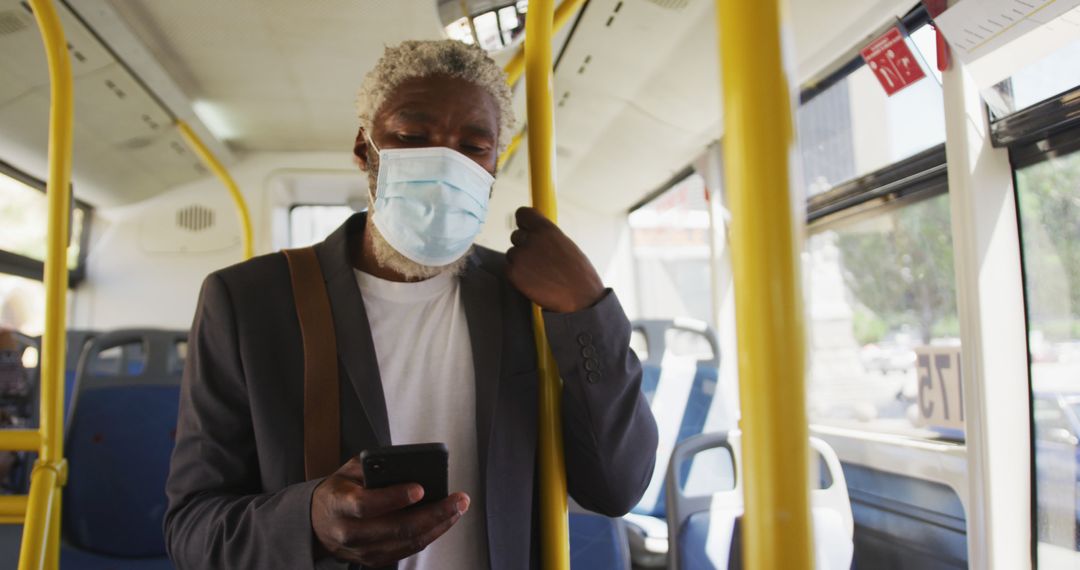 African american senior man wearing face mask using smartphone while standing in the bus - Free Images, Stock Photos and Pictures on Pikwizard.com