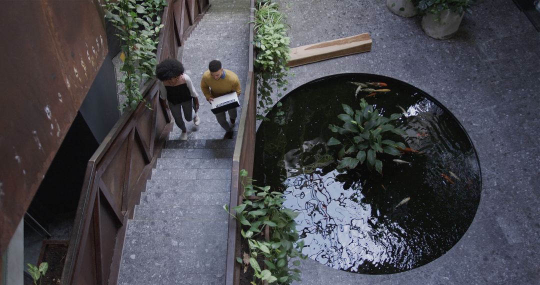 Professionals Walking Downstairs by Indoor Koi Pond with Plants - Free Images, Stock Photos and Pictures on Pikwizard.com