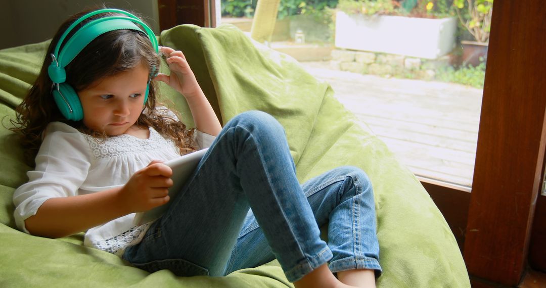 Young Girl Listening to Music with Headphones While Using Tablet on Bean Bag - Free Images, Stock Photos and Pictures on Pikwizard.com