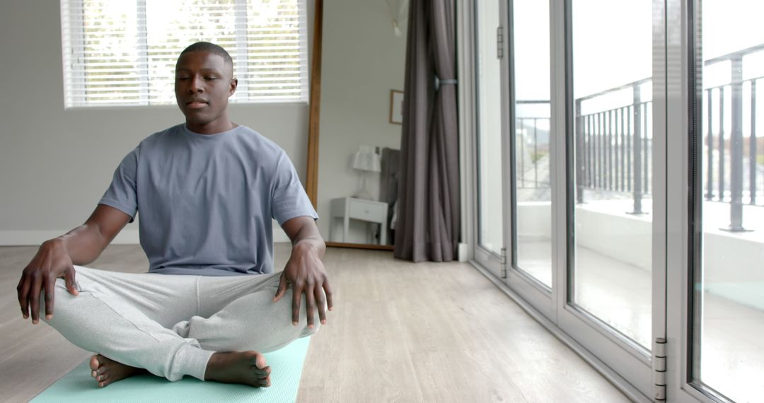 Man Meditating in Modern Living Room with Large Windows - Free Images, Stock Photos and Pictures on Pikwizard.com