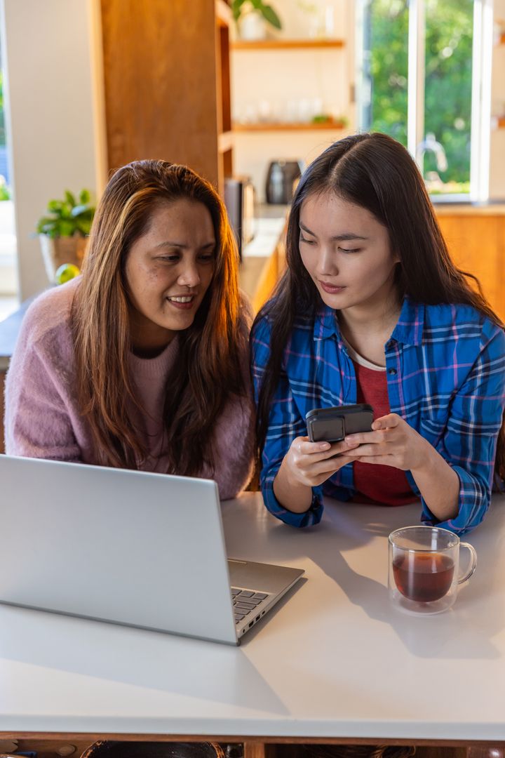 Mother and Daughter Connecting Digital Devices in Cozy Kitchen