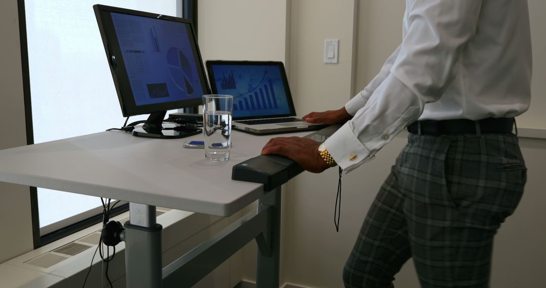 Businessman Working at Standing Desk with Laptops and Charts - Free Images, Stock Photos and Pictures on Pikwizard.com