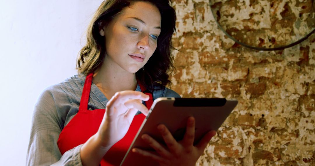 Young Woman in Red Apron Using Tablet in Cafe - Free Images, Stock Photos and Pictures on Pikwizard.com