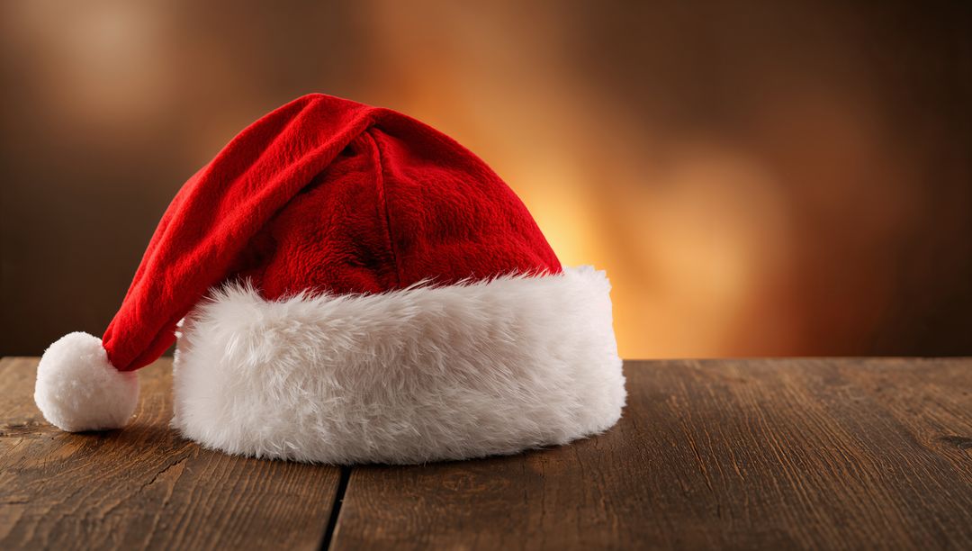 Red Santa hat resting on rustic wooden table with warm bokeh and plush white fur trim