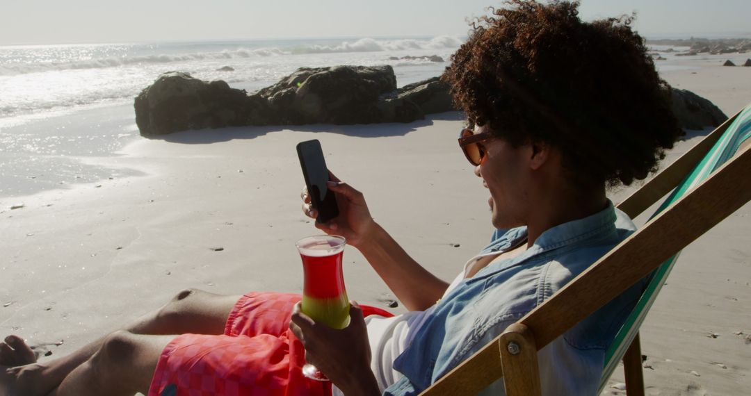 Young Man Relaxing on Beach Chair with Drink and Phone - Free Images, Stock Photos and Pictures on Pikwizard.com