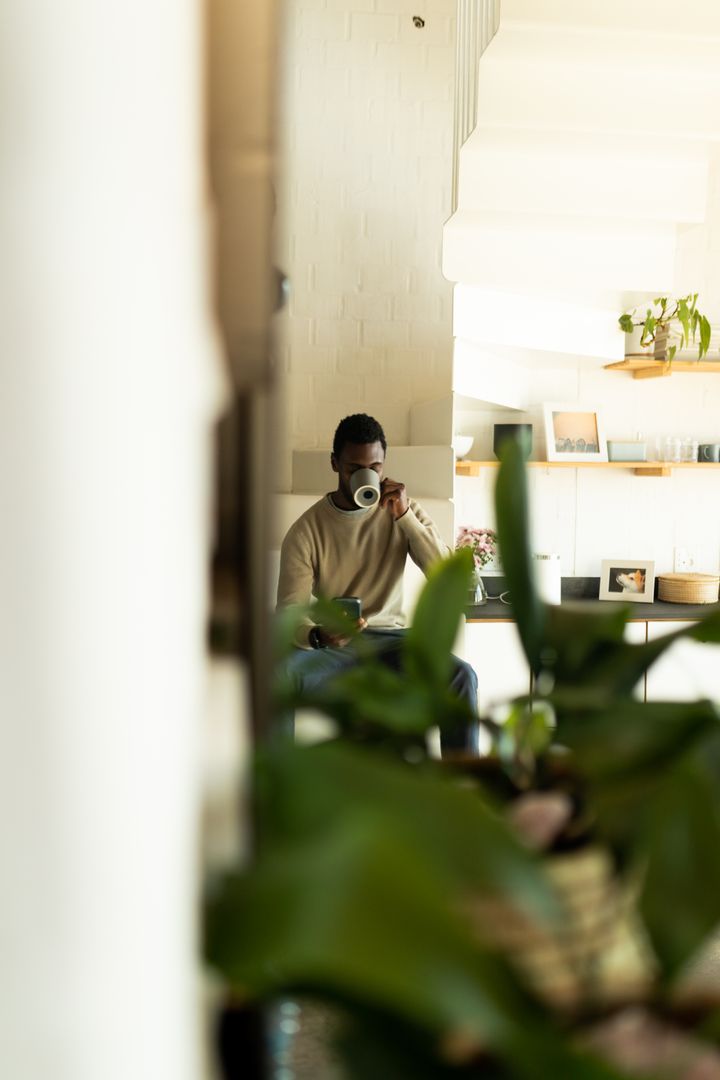 African American Man Drinking Coffee and Using Smartphone at Home - Free Images, Stock Photos and Pictures on Pikwizard.com