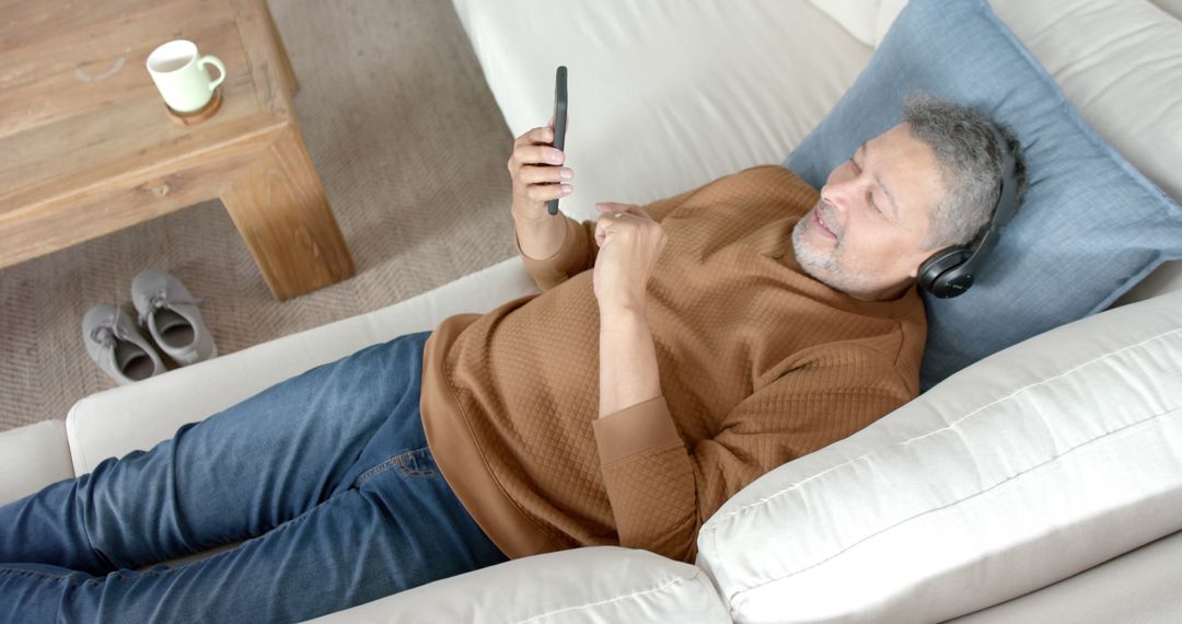 Middle-aged Man Relaxing on Couch with Headphones and Smartphone - Free Images, Stock Photos and Pictures on Pikwizard.com