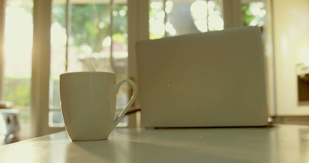 Steaming Coffee Mug and Laptop on Kitchen Table with Morning Sunlight - Free Images, Stock Photos and Pictures on Pikwizard.com