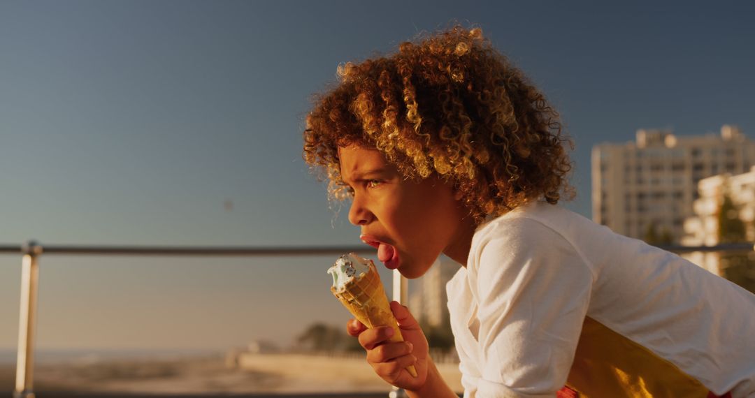 Curly-haired Child Enjoying Ice Cream Cone at Sunset by the Sea - Free Images, Stock Photos and Pictures on Pikwizard.com