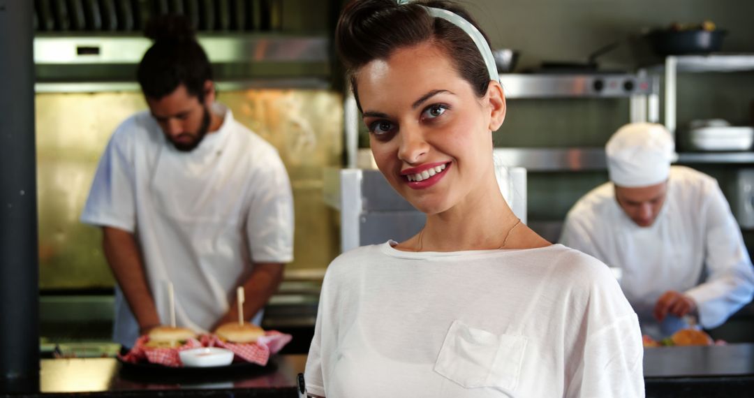 Smiling Waitress Stands in Restaurant Kitchen with Busy Chefs - Free Images, Stock Photos and Pictures on Pikwizard.com