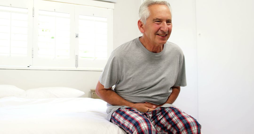 Elderly man smiling while sitting on bed in vibrant checkered pajamas - Free Images, Stock Photos and Pictures on Pikwizard.com