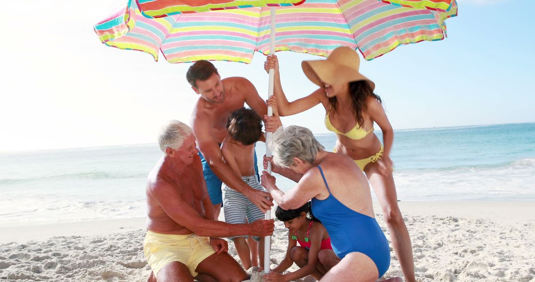 Multigenerational Family Enjoying Beach Day Under Colorful Umbrella - Free Images, Stock Photos and Pictures on Pikwizard.com