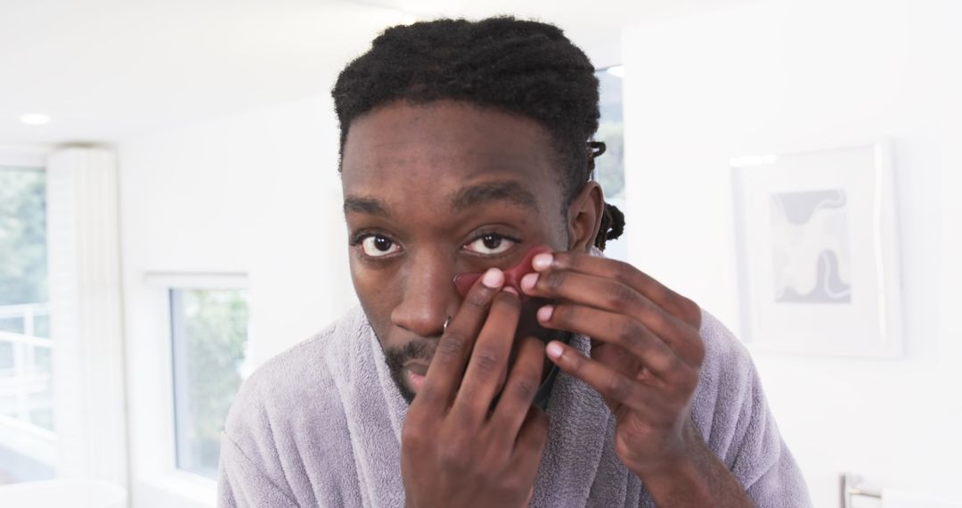 African American man removing contact lens in bathroom mirror during morning grooming routine