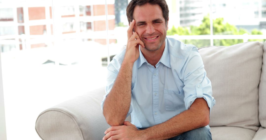 Cheerful man sitting on sofa in modern living room - Free Images, Stock Photos and Pictures on Pikwizard.com