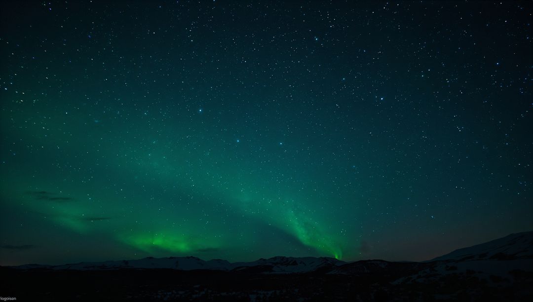 Emerald aurora borealis glowing over snowy tundra and mountain silhouettes under starry sky