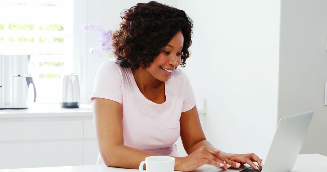 Smiling African American Woman Typing on Laptop at Home in Bright Kitchen - Free Images, Stock Photos and Pictures on Pikwizard.com