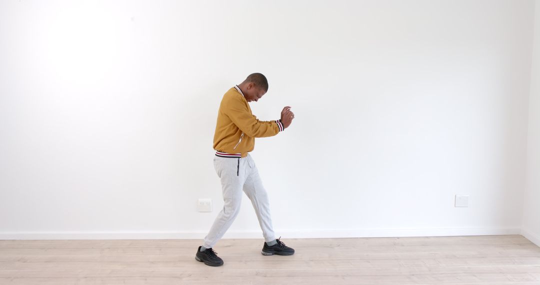Man Dancing Energetically in Casual Attire Against White Wall